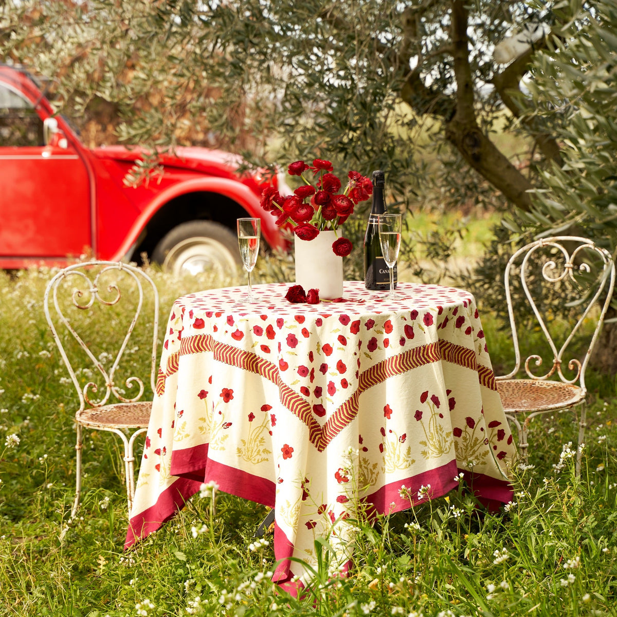Front view of French Tablecloth Poppies showcasing red poppy pattern and striped border on an outdoor dining table