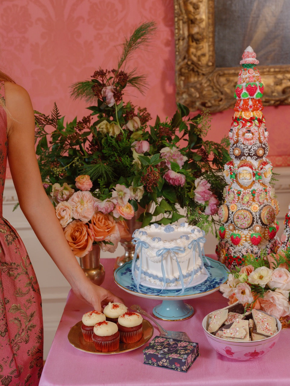 Festive dessert table with cakes, cookies, floral arrangements, and a decorated Christmas tree