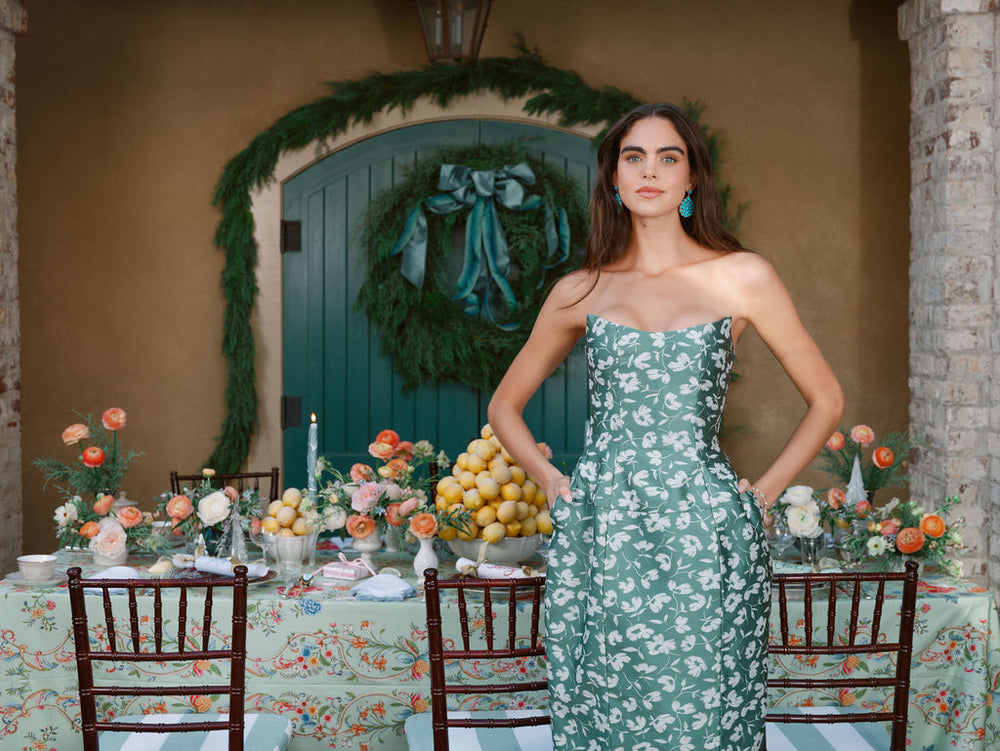 Woman wearing turquoise and diamond drop earrings standing before a floral tablescape and arched green door