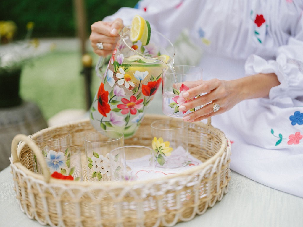 Person pours a citrus drink from a floral pitcher into a glass beside matching floral glassware