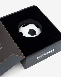 Football: The Impossible Collection by Assouline: angled overhead view of the open companion black box with matte black velvet interior; a standalone black-and-white soccer ball rests in a circular foam recess at center; FOOTBALL THE IMPOSSIBLE COLLECTION in white type on the front face of the exterior; the box lid is open at left