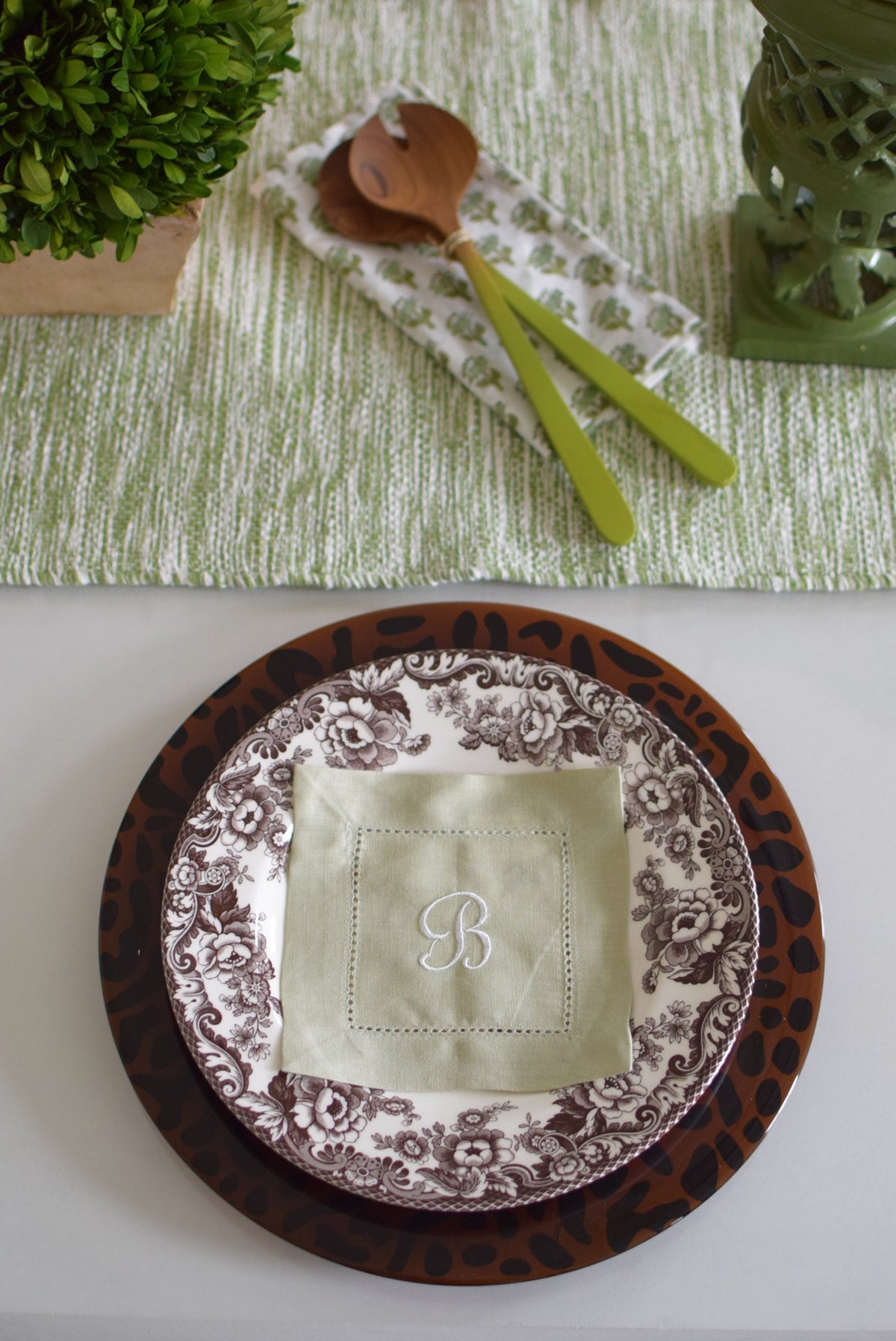 Top-down view of Cheetah charger plate showing brown glass with black cheetah-print rim beneath a floral dinner plate on a white table