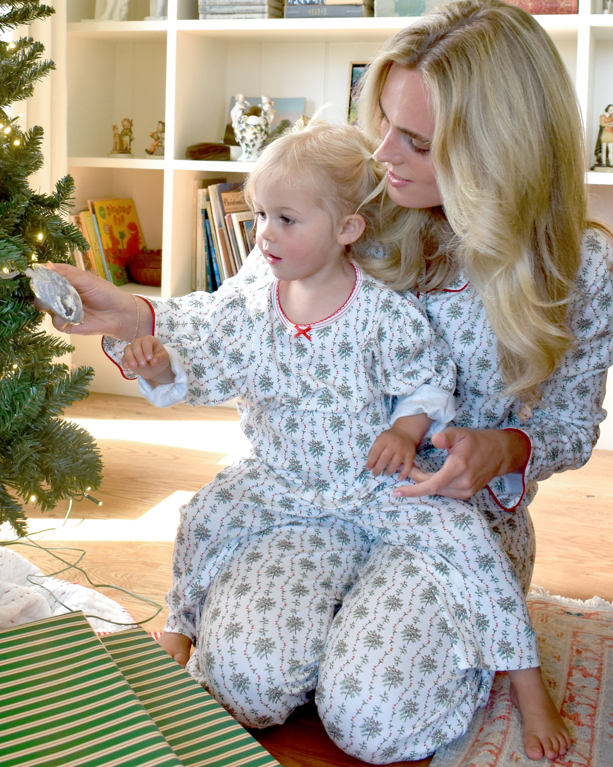 Woman and child decorating a Christmas tree together in floral pajamas
