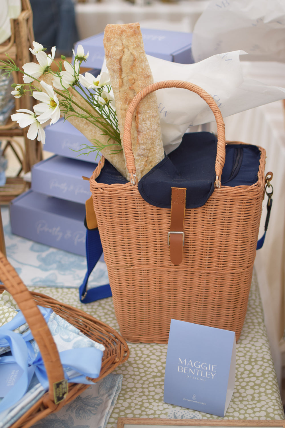 Front view of rattan picnic basket showcasing navy insulated lining and blue shoulder strap, filled with baguettes and white flowers