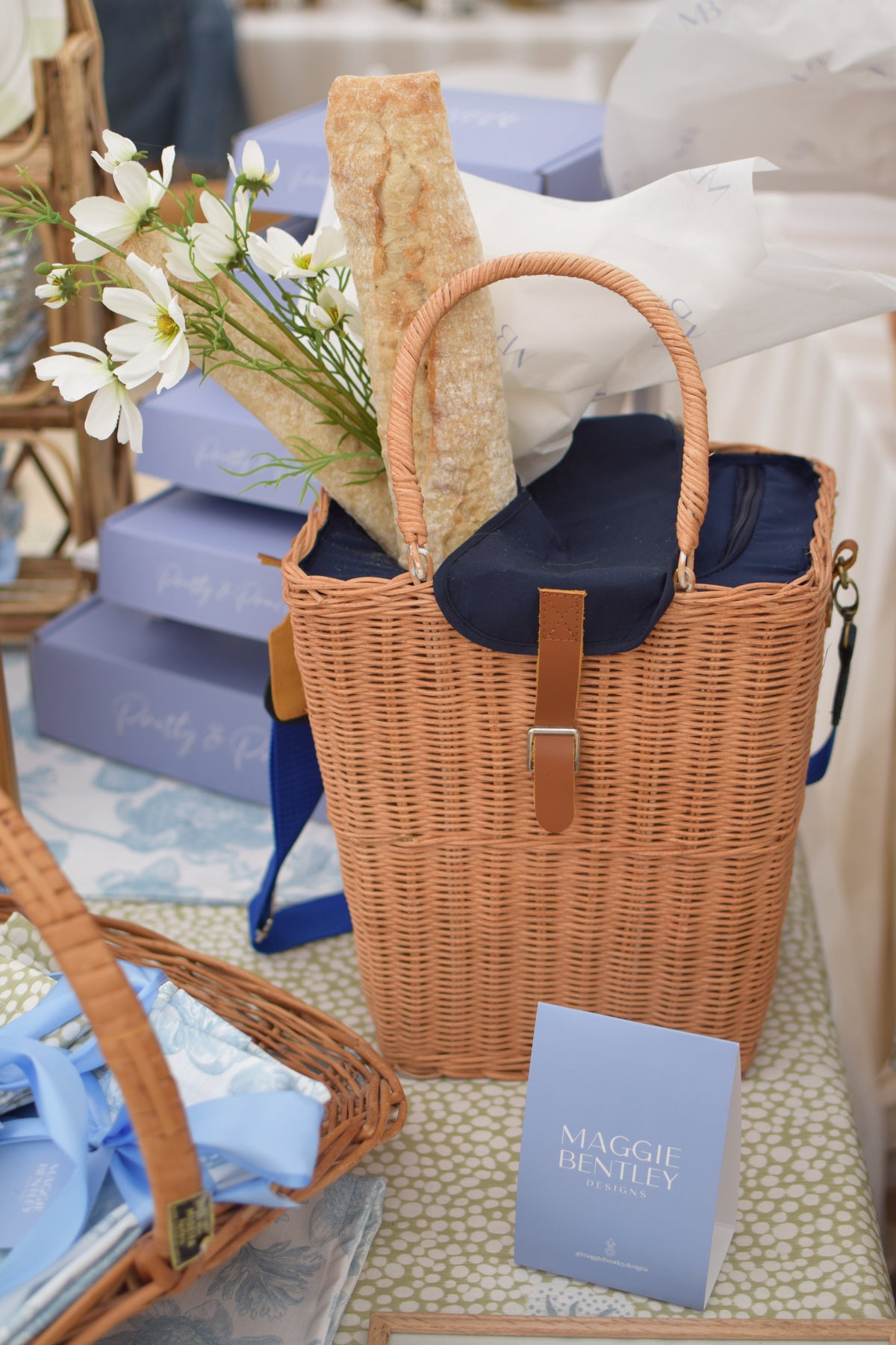 Front view of rattan picnic basket showcasing navy insulated lining and blue shoulder strap, filled with baguettes and white flowers