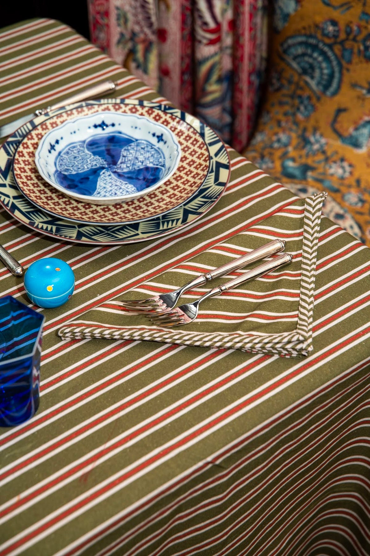 Top view of Isabelle napkin in Winter Stripe folded on table showing olive-green, red and white stripes and piped edge