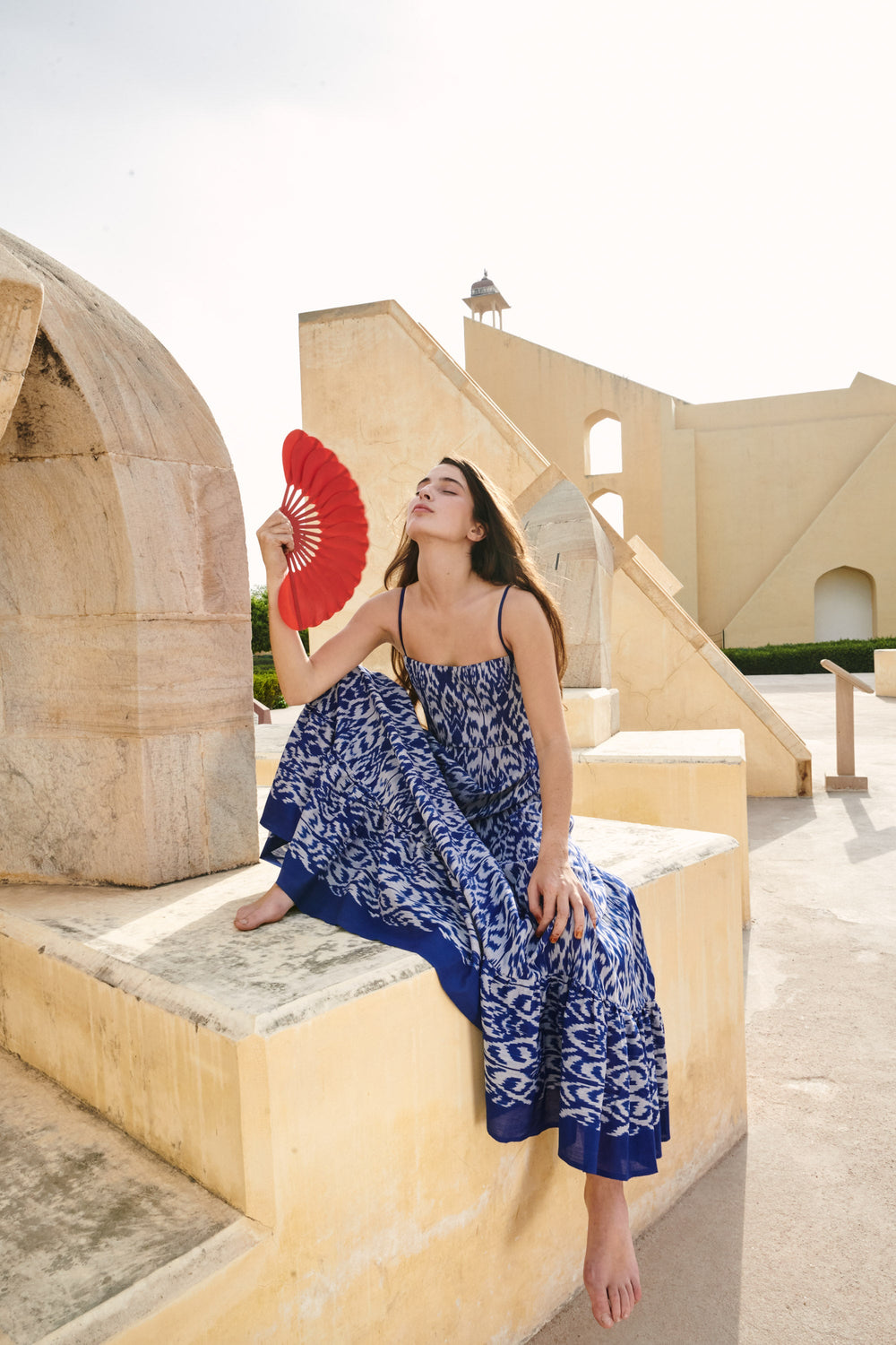 Three-quarter view of Aquarius dress on model, fitted corset top, blue ikat print, on sandstone terrace