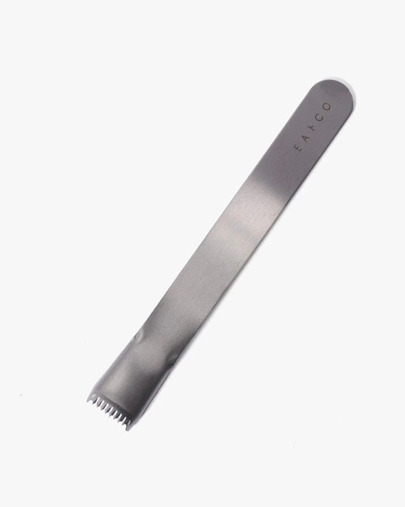 Angled view of EAtCo corn peeler showing stainless steel serrated blade and long slim handle on white background