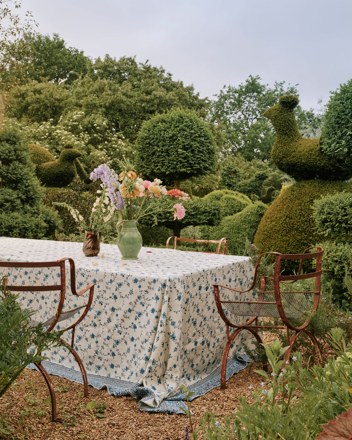 Tabletop view of D’Ascoli Malabar rectangular linen tablecloth with blue indigo floral print draped on outdoor table with vase