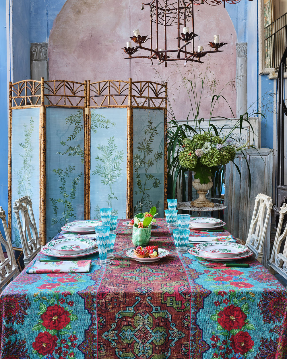 Tabletop view of D’Ascoli Scheherazad tablecloth showcasing ornate turquoise and red floral medallion pattern with place settings