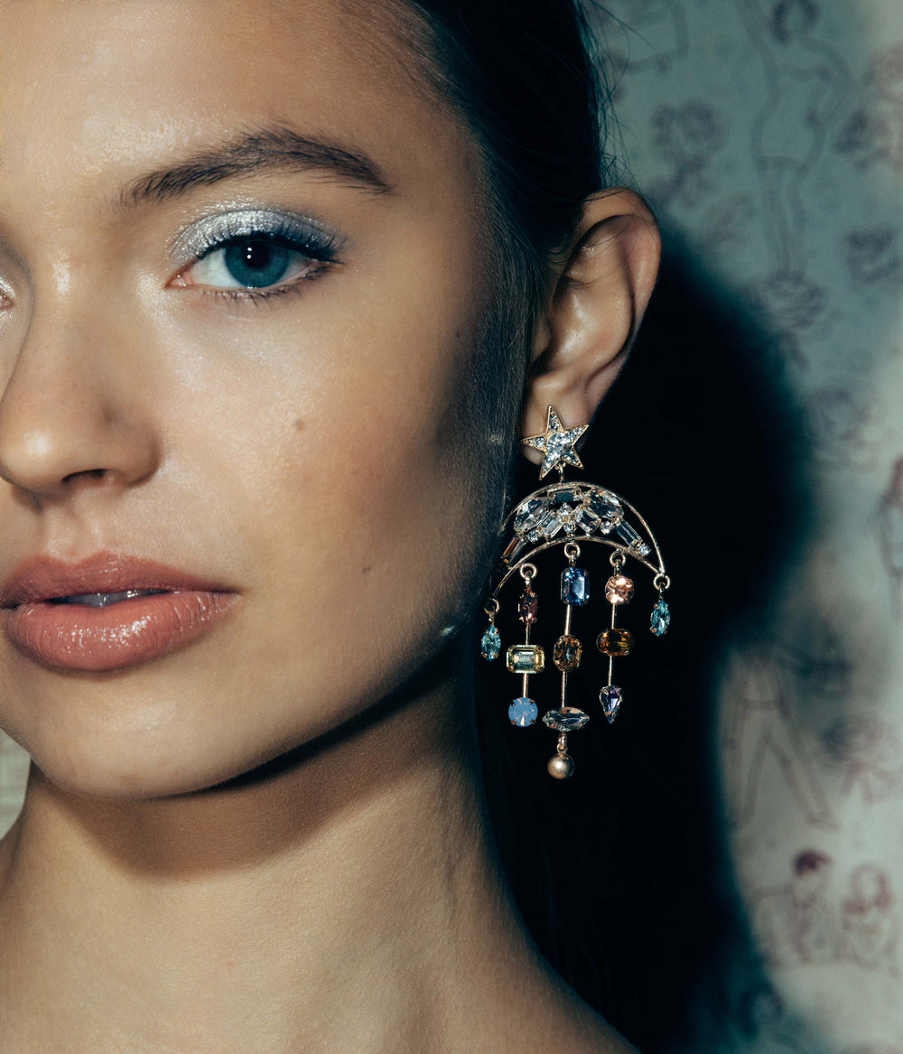 Close up of Daydreamer Earrings showcasing crescent moon top with dangling multicolored glass stones on model against patterned background