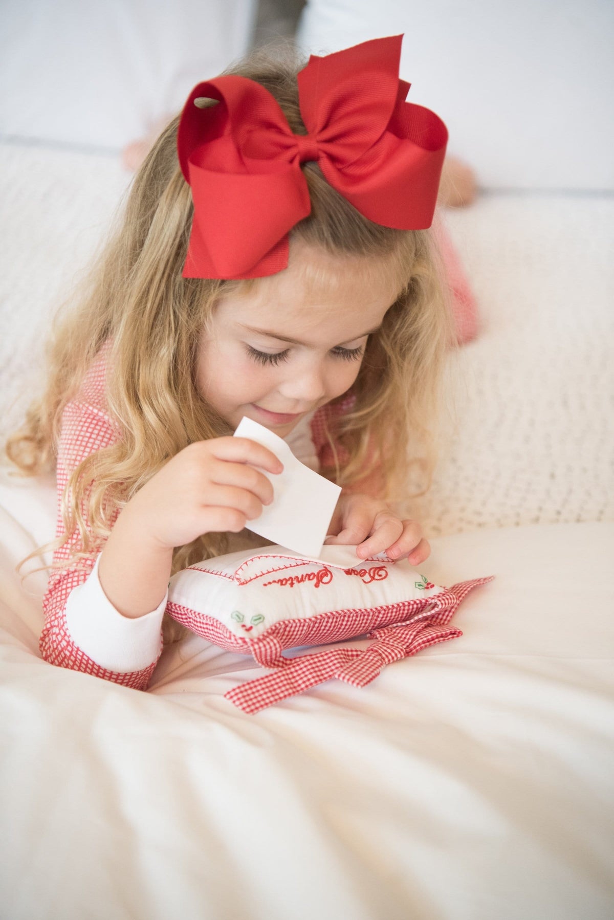 Child holding a letter with the red gingham Dear Santa Door Pillow on a bed