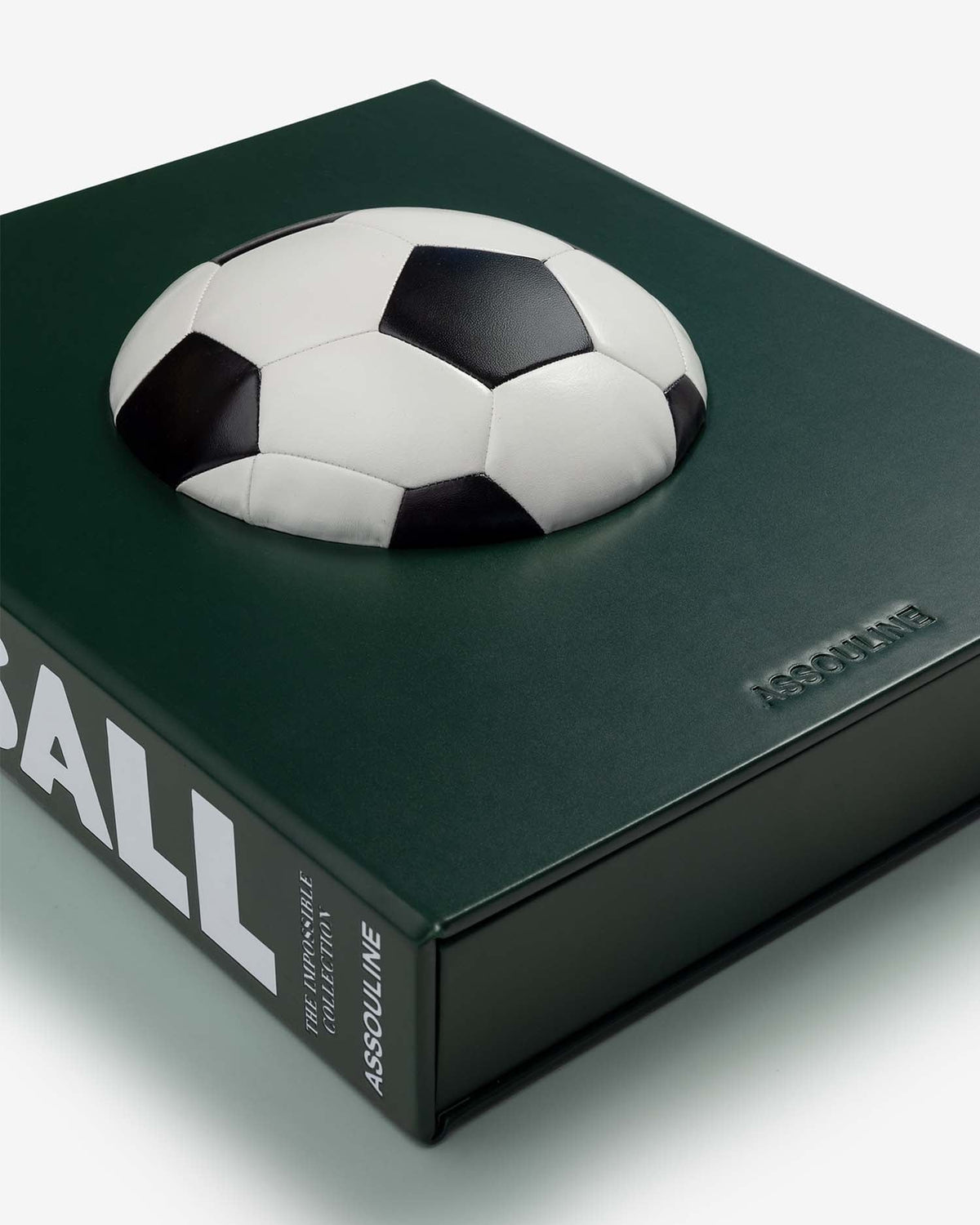 Football: The Impossible Collection by Assouline: angled overhead close-up of the slipcase lying flat; the three-dimensional black-and-white soccer ball rests on the dark forest green cover photographed from above; the lower spine shows ...BALL, THE IMPOSSIBLE COLLECTION, ASSOULINE in white; ASSOULINE embossed on the cover face at right; the green slipcase base and lid are visible