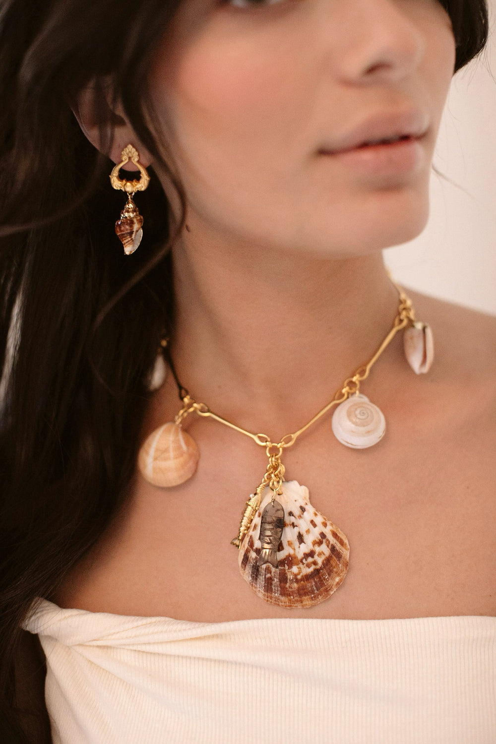 Close-up of Del Mar necklace on model showing 24K gold-plated chain with natural shells and smoky quartz fish charm