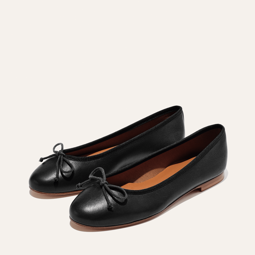 The Demi - Black Nappa by margaux-development are handmade in Spain, featuring comfortable black nappa leather, round toes, small bows, brown insoles, and flat brown soles, shown on a neutral background.