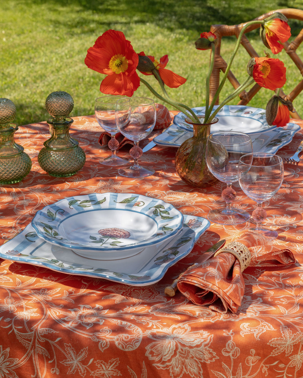 Orange linen napkins styled on a floral table setting with red poppies, glassware, and blue floral dishes