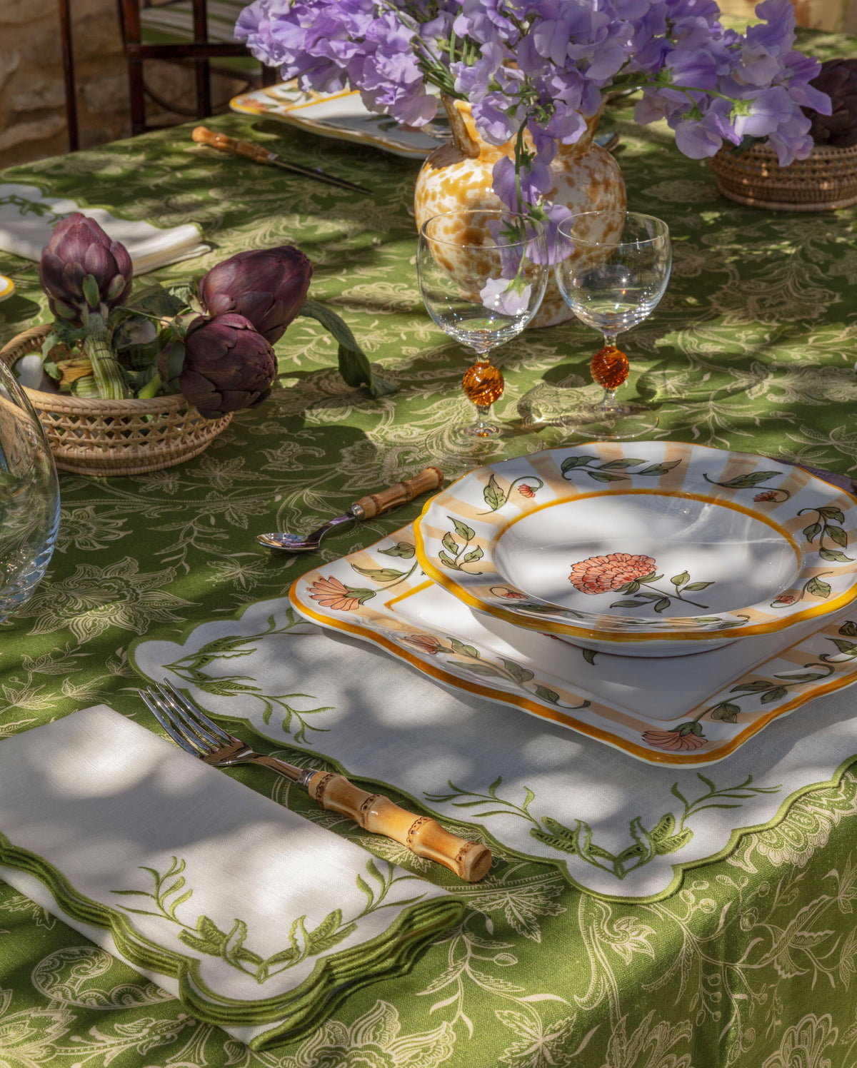 Yellow square soup plate on a floral table setting with flowers, glassware, and serving dishes