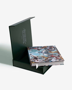 Football: The Impossible Collection by Assouline: angled view of the open black hinged box with the book partially extracted; the book cover shows a full-color Baroque-style classical painting featuring footballers playing among clouds and classical columns; the inside of the matte black box lid shows a quote in white text; a white ribbon bookmark trails from the book