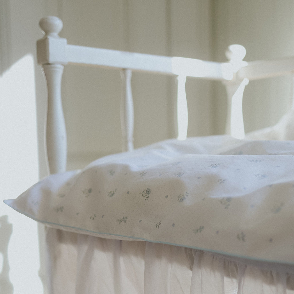 White baby duvet with floral pattern on a white bed in a softly lit room
