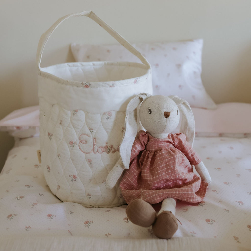 Cot with a quilted basket and plush toy on a bed with floral bedding.