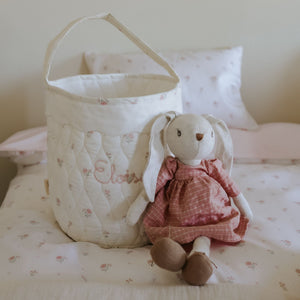 Cot with a quilted basket and plush toy on a bed with floral bedding.