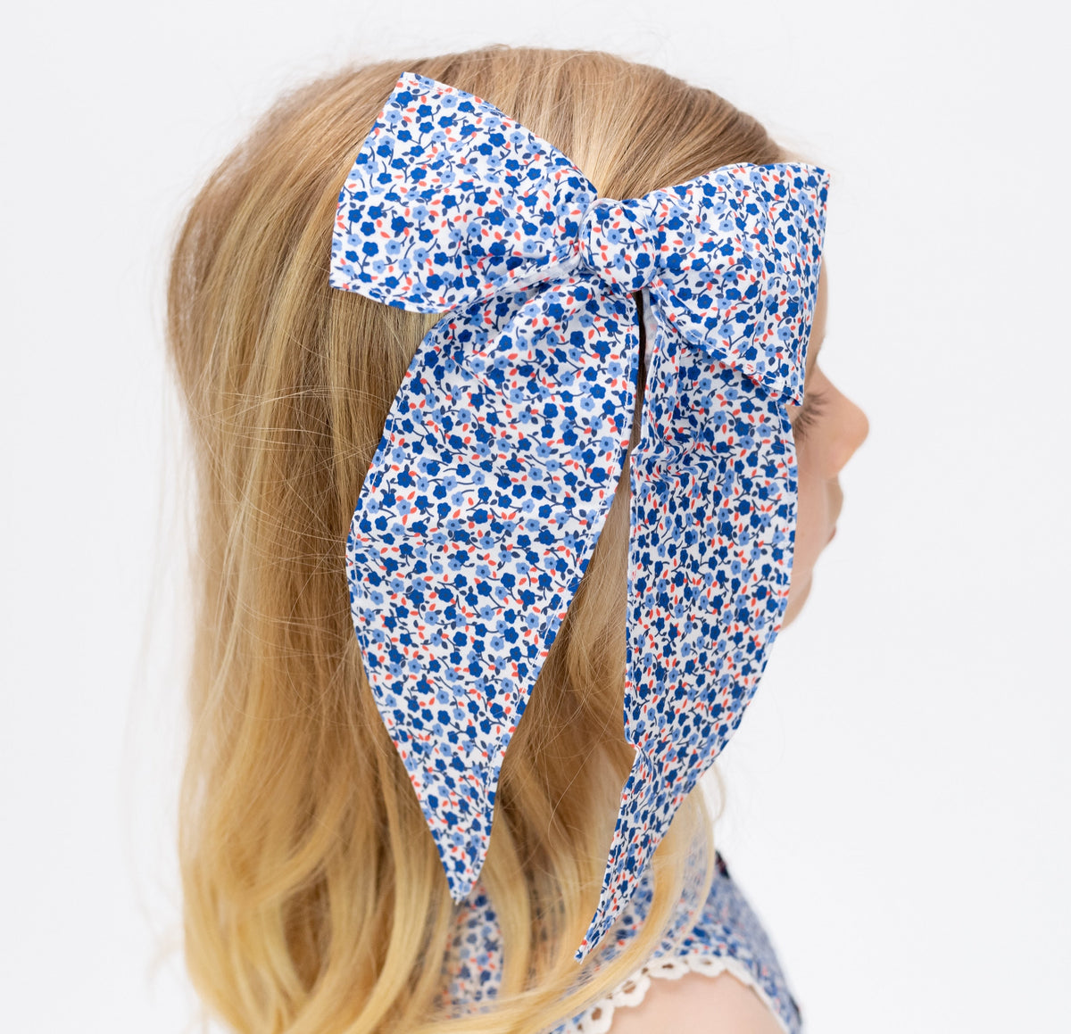 Close-up of Abigail Bow showcasing its vibrant red, white, and blue floral print on a child’s hair against a white background