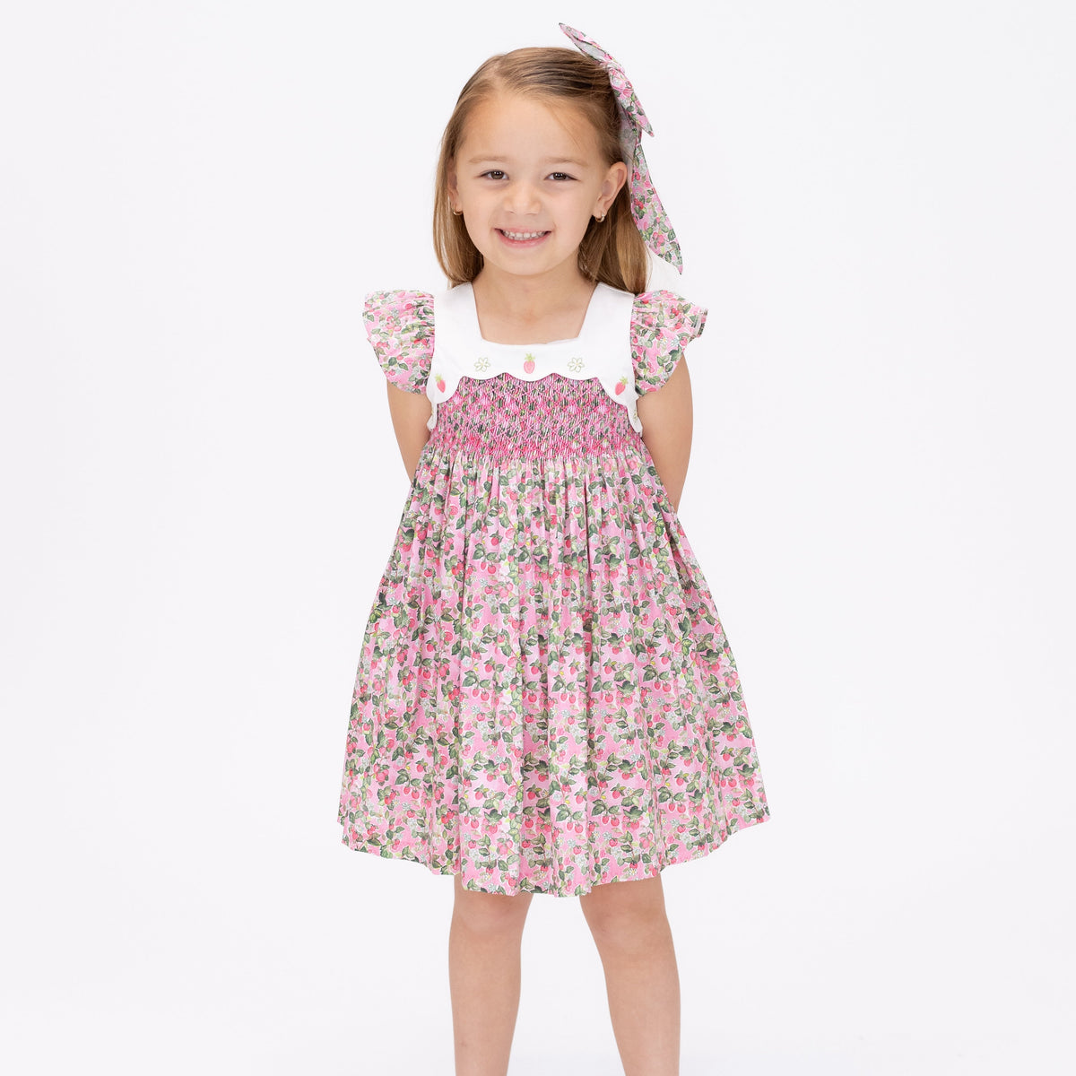 Front view of Strawberry Patch Girl Dress with pink hand-smocked chest, flutter sleeves, and strawberry print