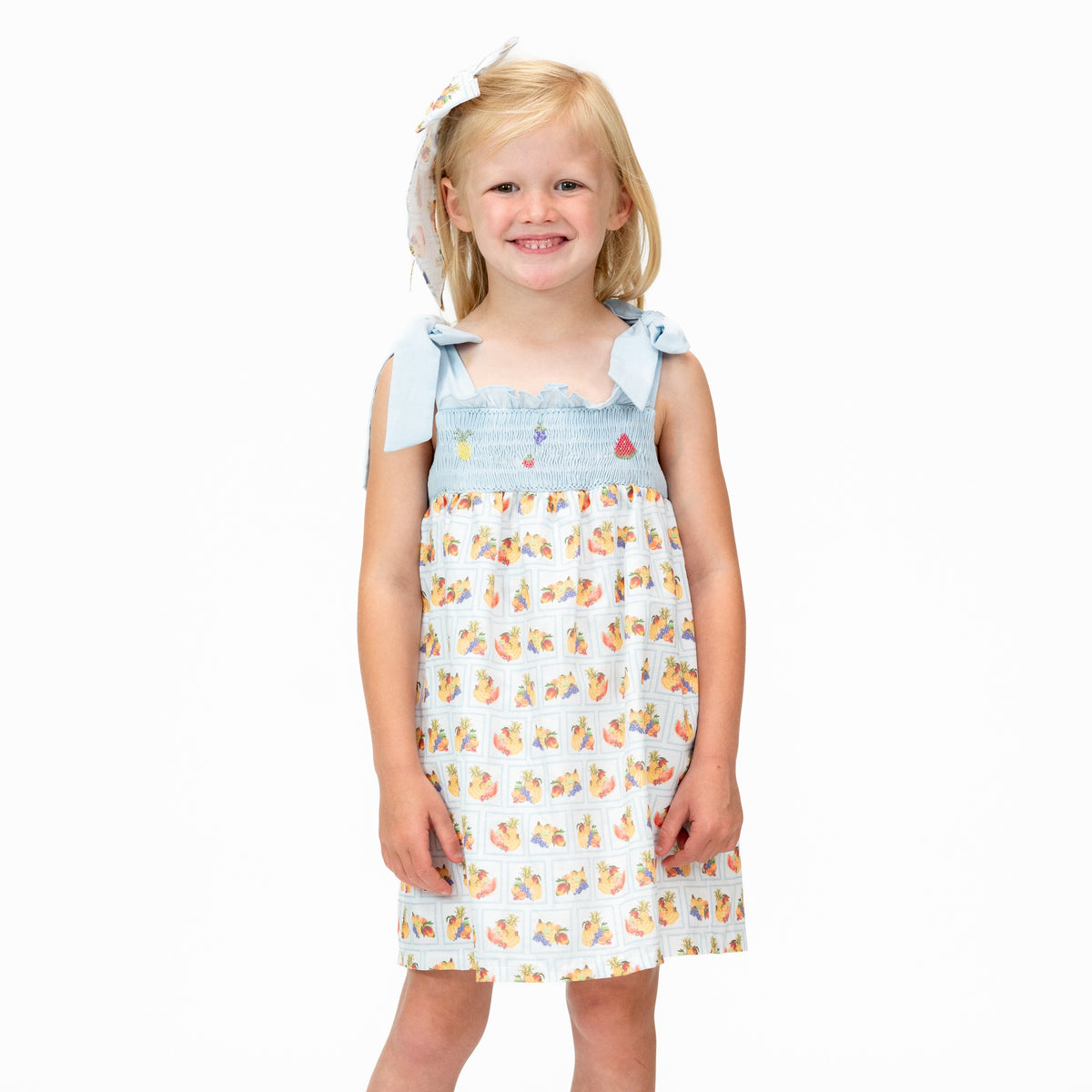 Front view of Tropicale Girl Dress showcasing fruit embroidery and adjustable bow straps on a child against a white background