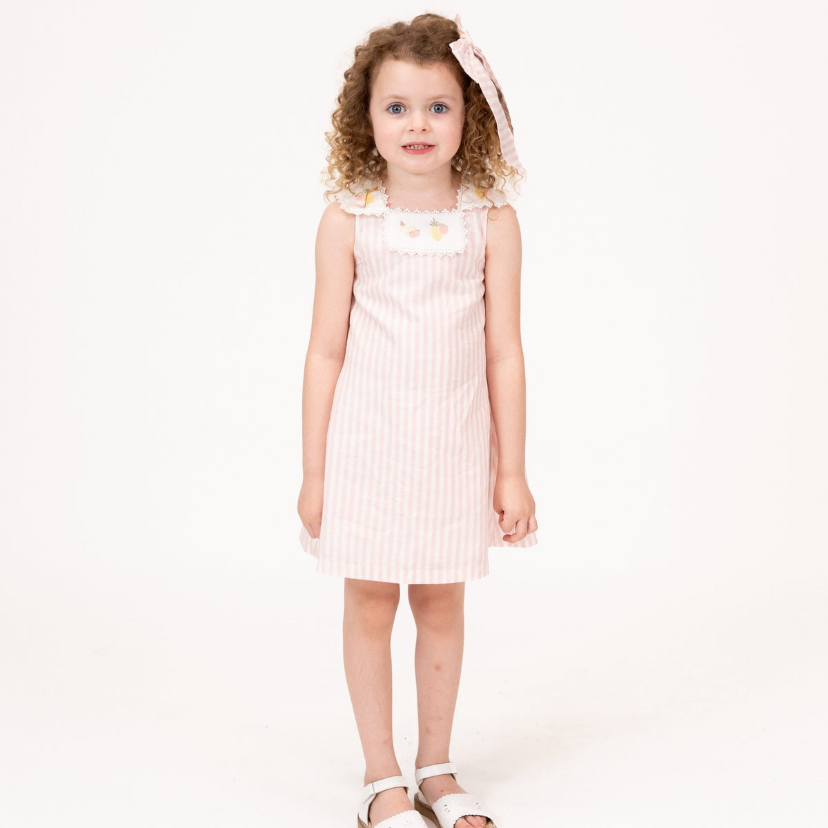 Front view of Ananas Girl Dress showcasing pink and white stripes and embroidered fruit bib on child against white background