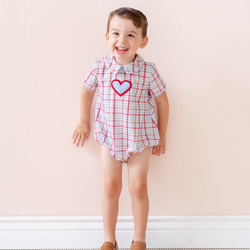 Front view of Romeo Boy Bubble romper showcasing Peter Pan collar, red heart appliqué and red-and-blue plaid on pale pink background