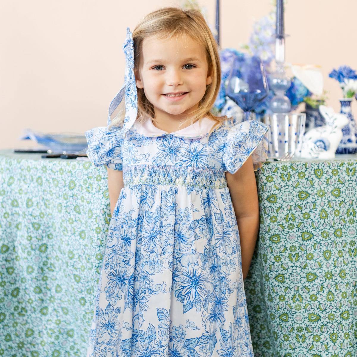 Front view of Beatrix Bow showcasing its white base with blue floral accents on a girl wearing a matching floral dress