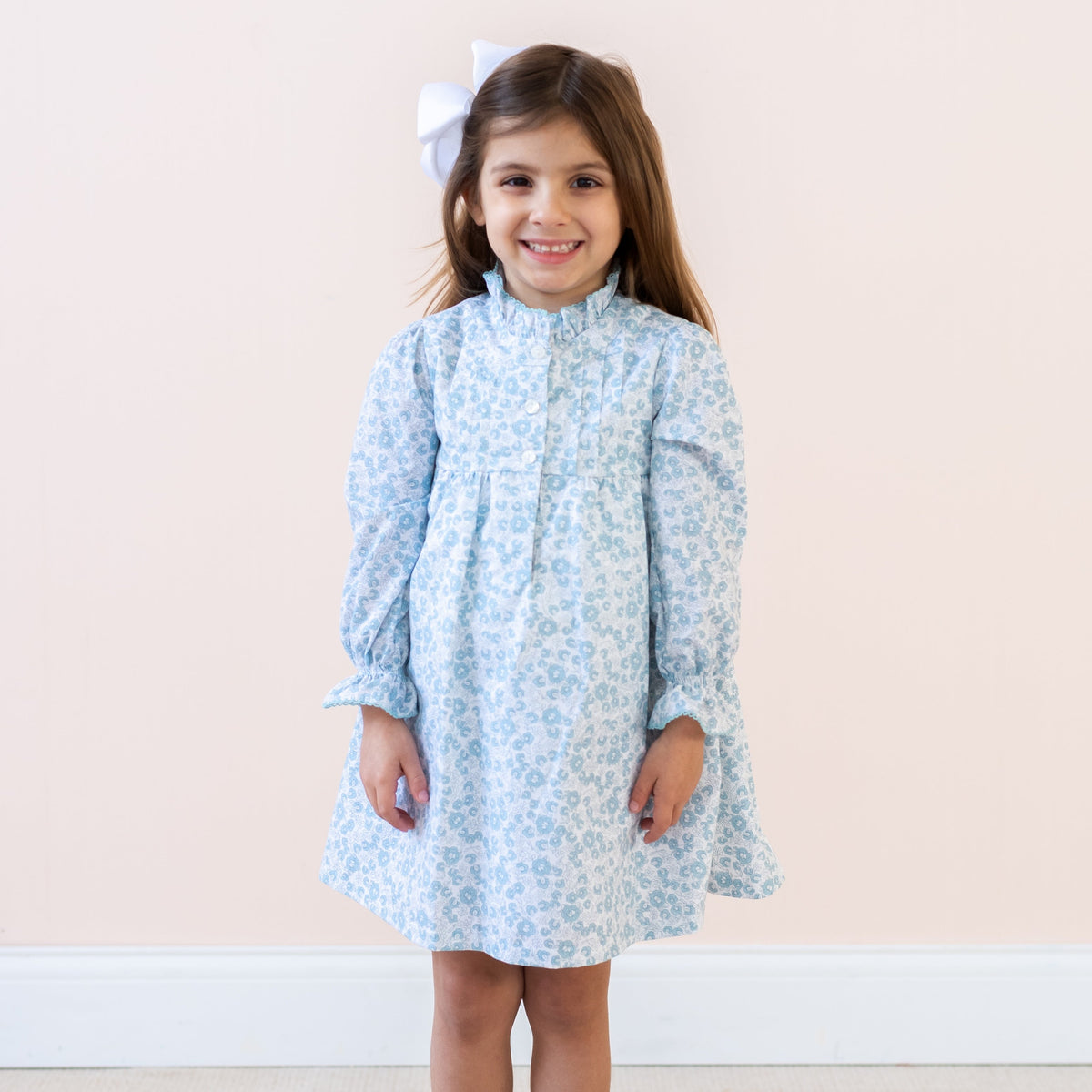 Front view of Victoria girl dress worn by a child, blue floral print with ruffle collar and sleeves, pale pink background