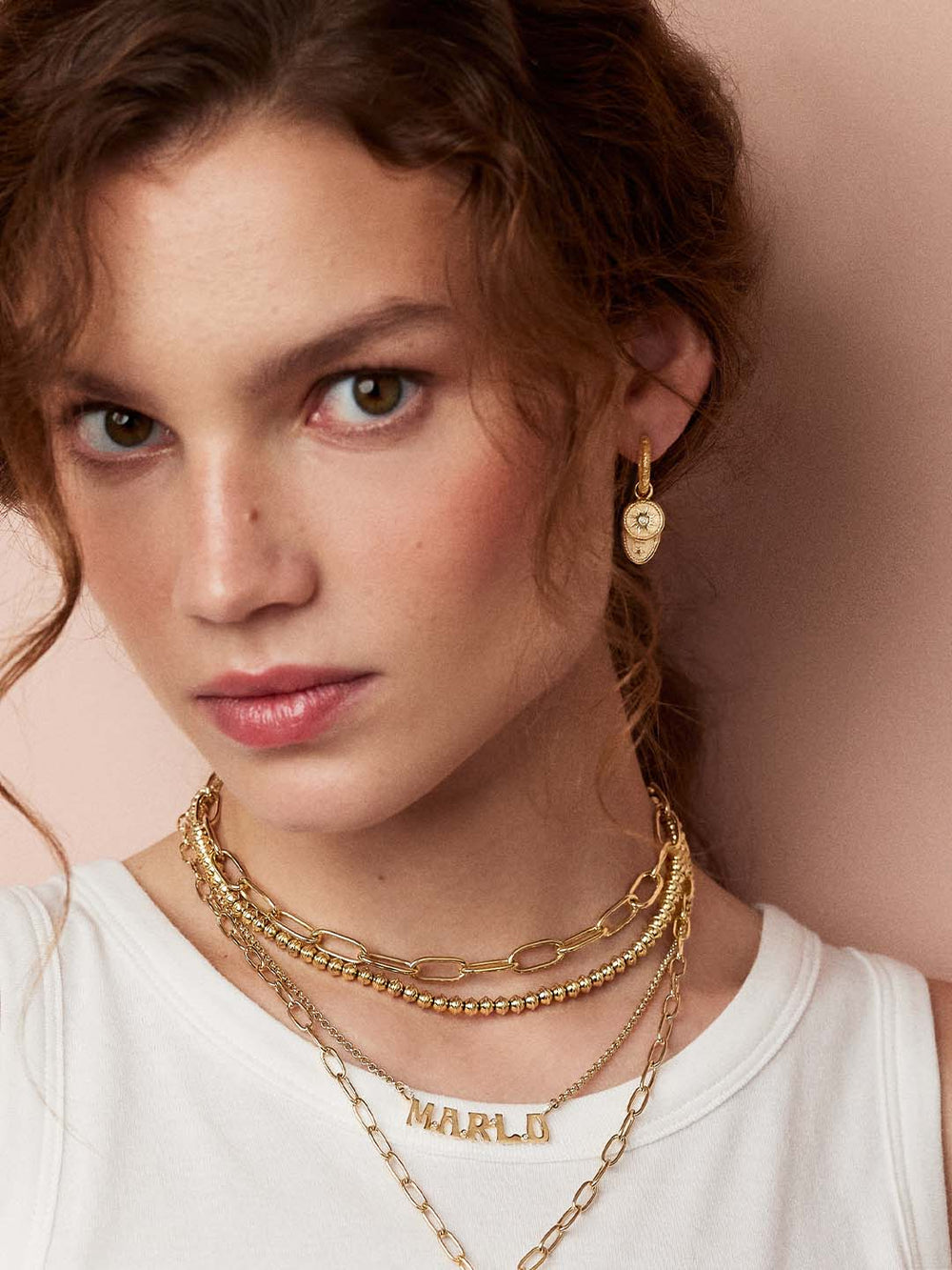 Close-up of Mixed Southwestern Hoops on model, 14k gold hoop layered with removable embroidered charm on pink background