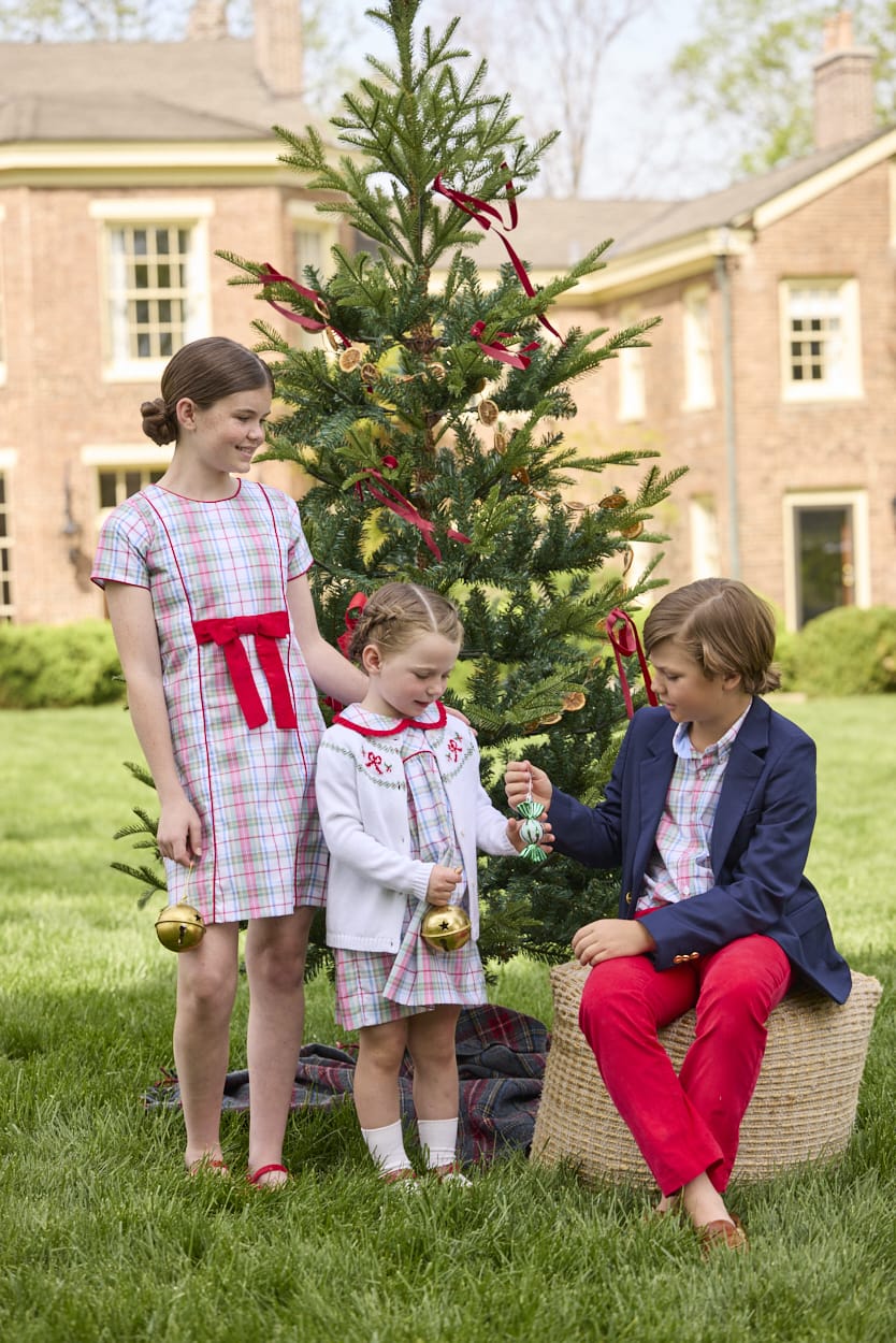 Little English classic children's clothing. Girls A-line Cora Dress in red and green plaid with red bow and red piping detail for the holidays.  Boys Douglas Plaid button down shirt with red corduroy pants and navy wool blazer. Toddler girls Eleanor Dress - Douglas Plaid with ruffled peter pan collar and tie sash in back paired with white Holiday Bow Fair Isle Cardigan