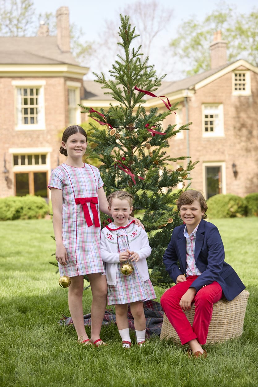 Little English classic children's clothing. Girls A-line Cora Dress in red and green plaid with red bow and red piping detail for the holidays.  Boys Douglas Plaid button down shirt with red corduroy pants and navy wool blazer. Toddler girls Eleanor Dress - Douglas Plaid with ruffled peter pan collar and tie sash in back paired with white Holiday Bow Fair Isle Cardigan