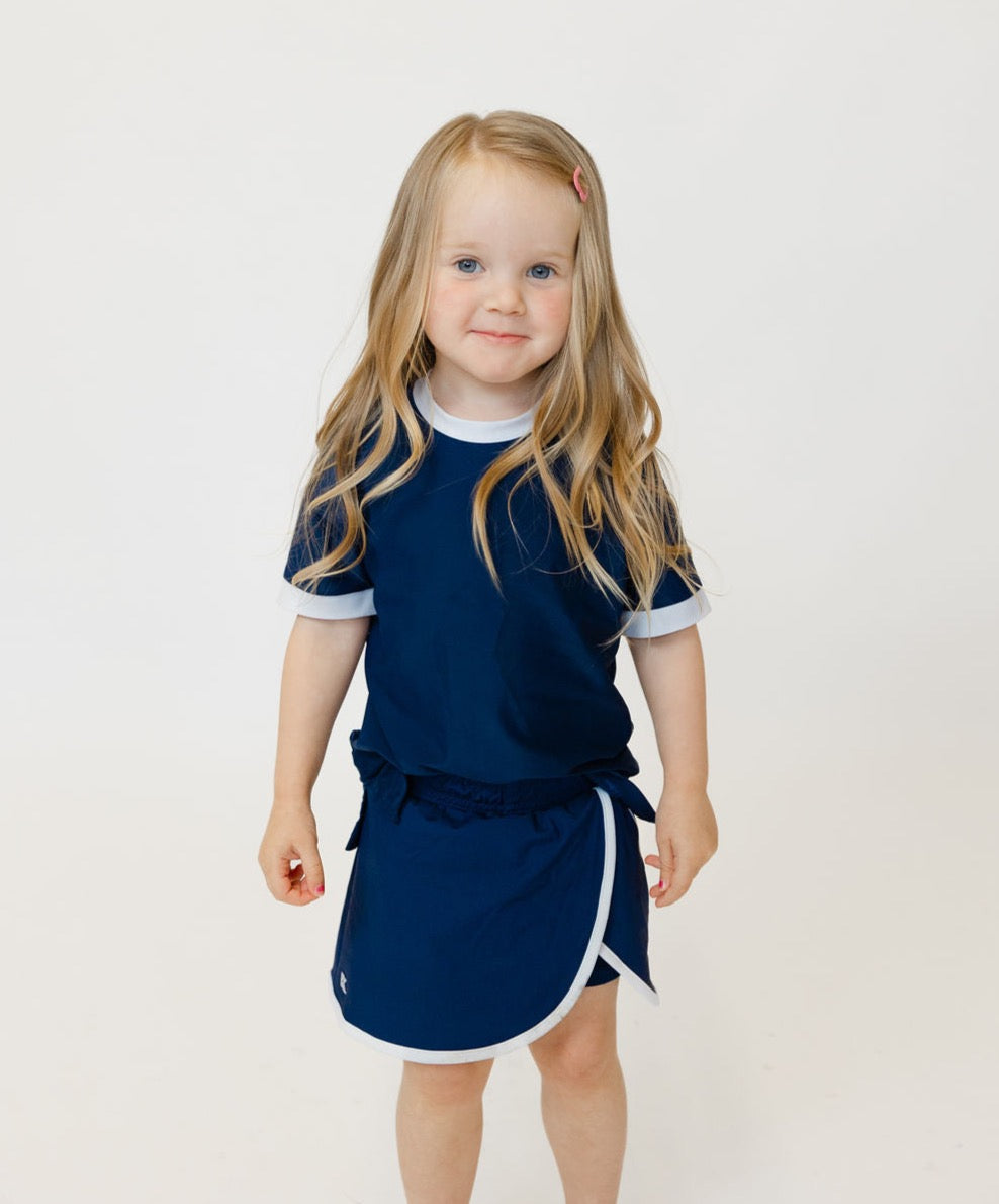Front view of Power Skort in navy on a toddler showing A-line silhouette, elastic waistband, built-in shorts and white trim on plain white background