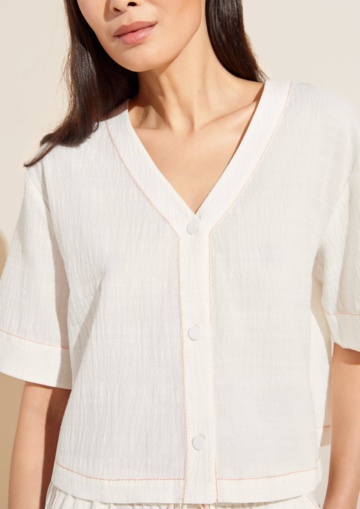 Front view of crinkle woven short-sleeve top in ivory with canyon-sunset contrast embroidery stitch and covered buttons