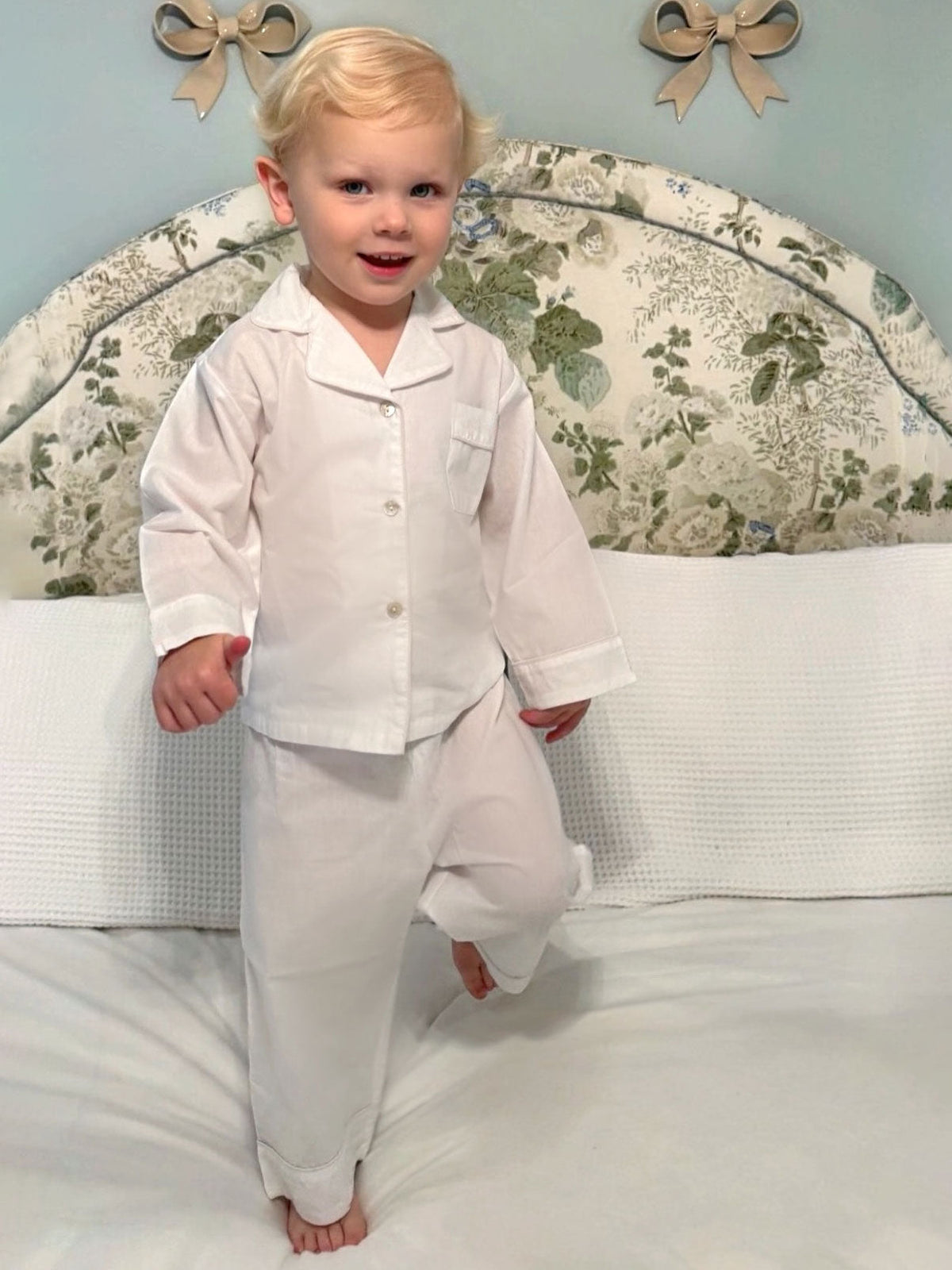 Front view of Harper 2-piece white pants set on toddler model showing long-sleeve top and relaxed pants on bed