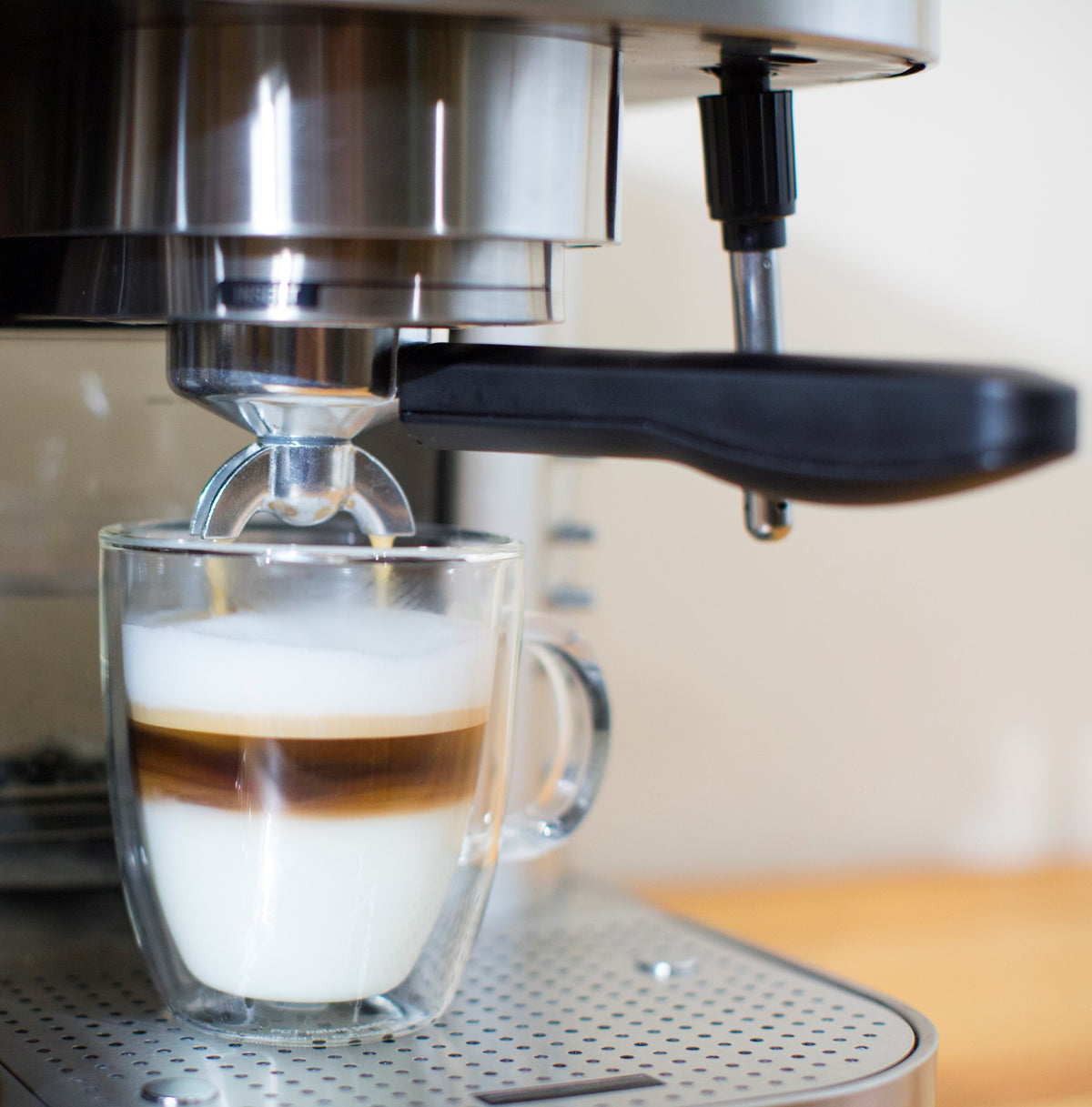 Automatic pump espresso machine brewing espresso into a glass cup on a kitchen counter