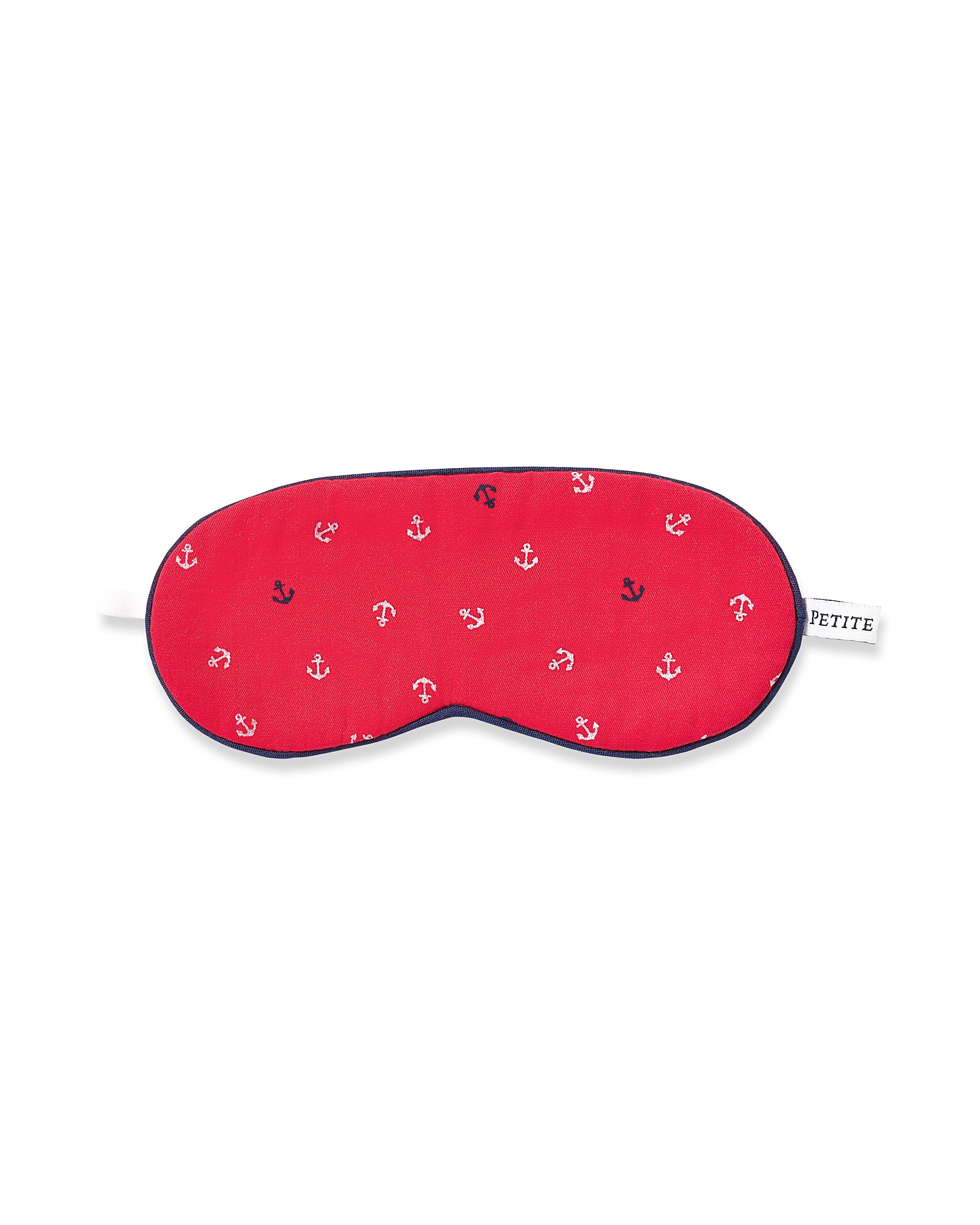 The Kids Twill Sleep Mask in Anchors Away by Petite Plume features red fabric with white anchor patterns, navy trim, a white strap, and a PETITE side tag. Its an ideal accessory for kids wearing red pajamas dreaming of nautical adventures.