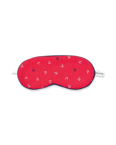 The Kids Twill Sleep Mask in Anchors Away by Petite Plume features red fabric with white anchor patterns, navy trim, a white strap, and a PETITE side tag. Its an ideal accessory for kids wearing red pajamas dreaming of nautical adventures.