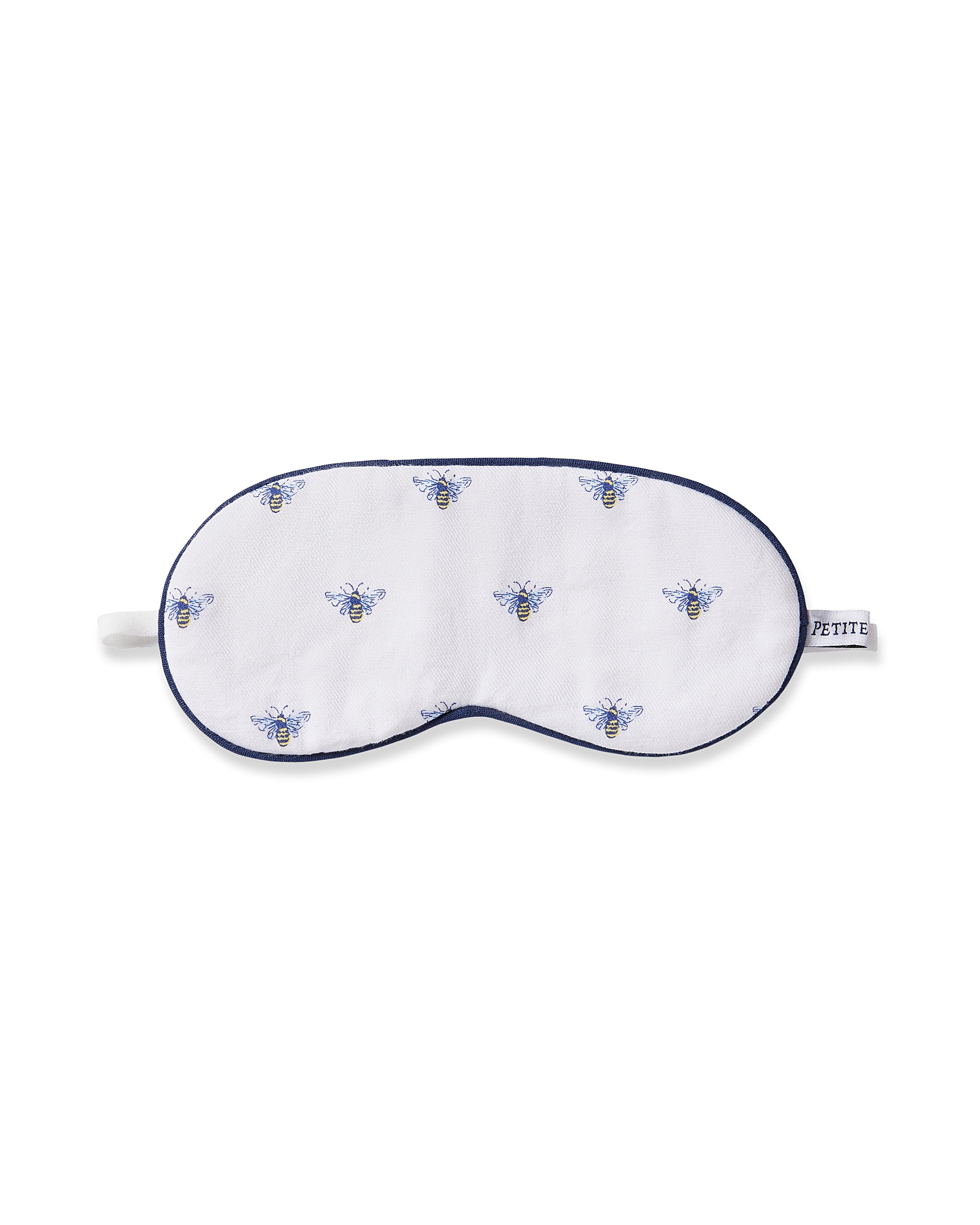 The Petite Plume Kids Twill Sleep Mask in Buzzing Bees is a white mask with blue and yellow bees pattern, dark blue trim, an elastic strap for comfort, and offers monogramming for personalization.