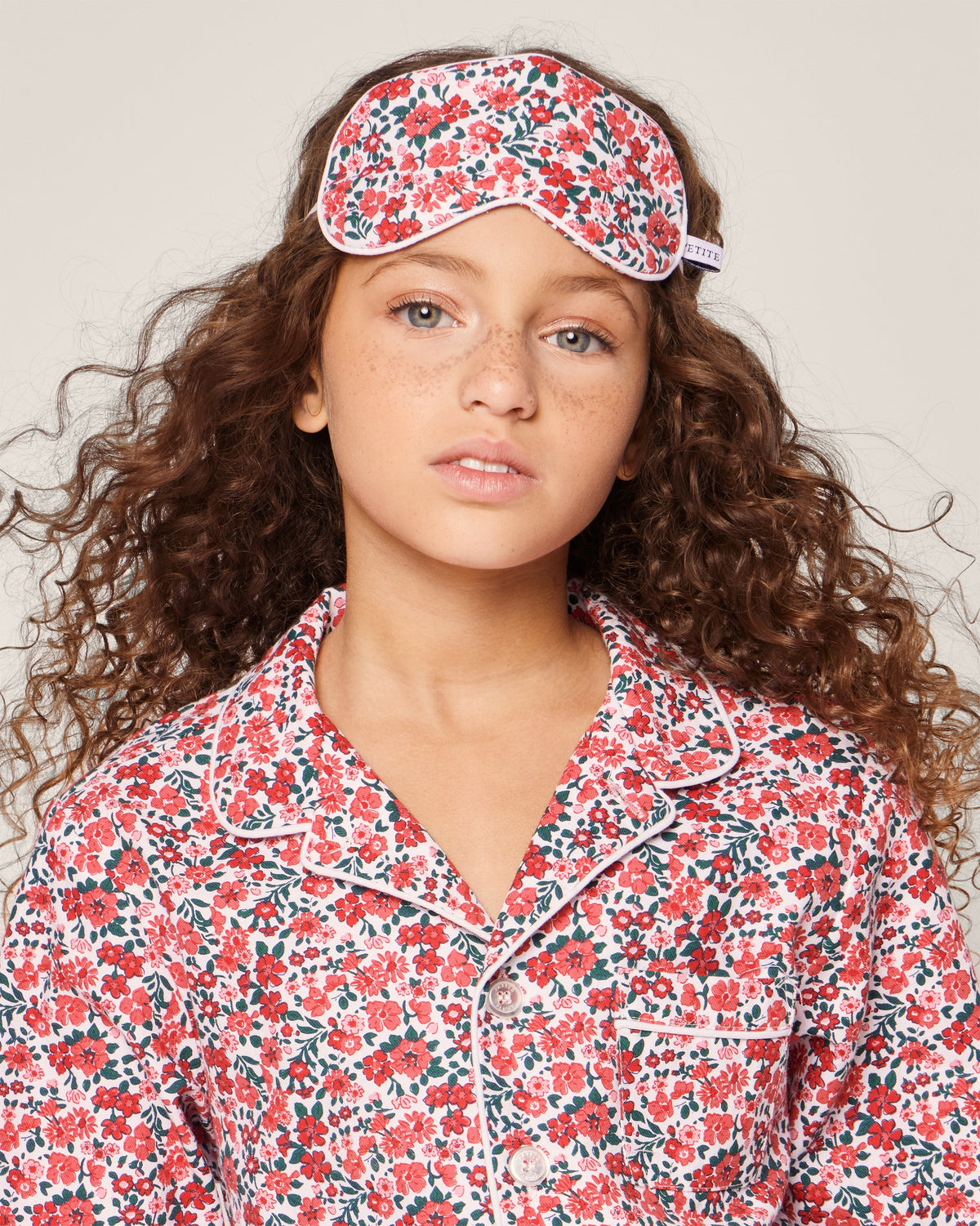 Front view of Kid’s Twill Sleep Mask in Fleurs des Bois showing floral print and piping on a child against a neutral background