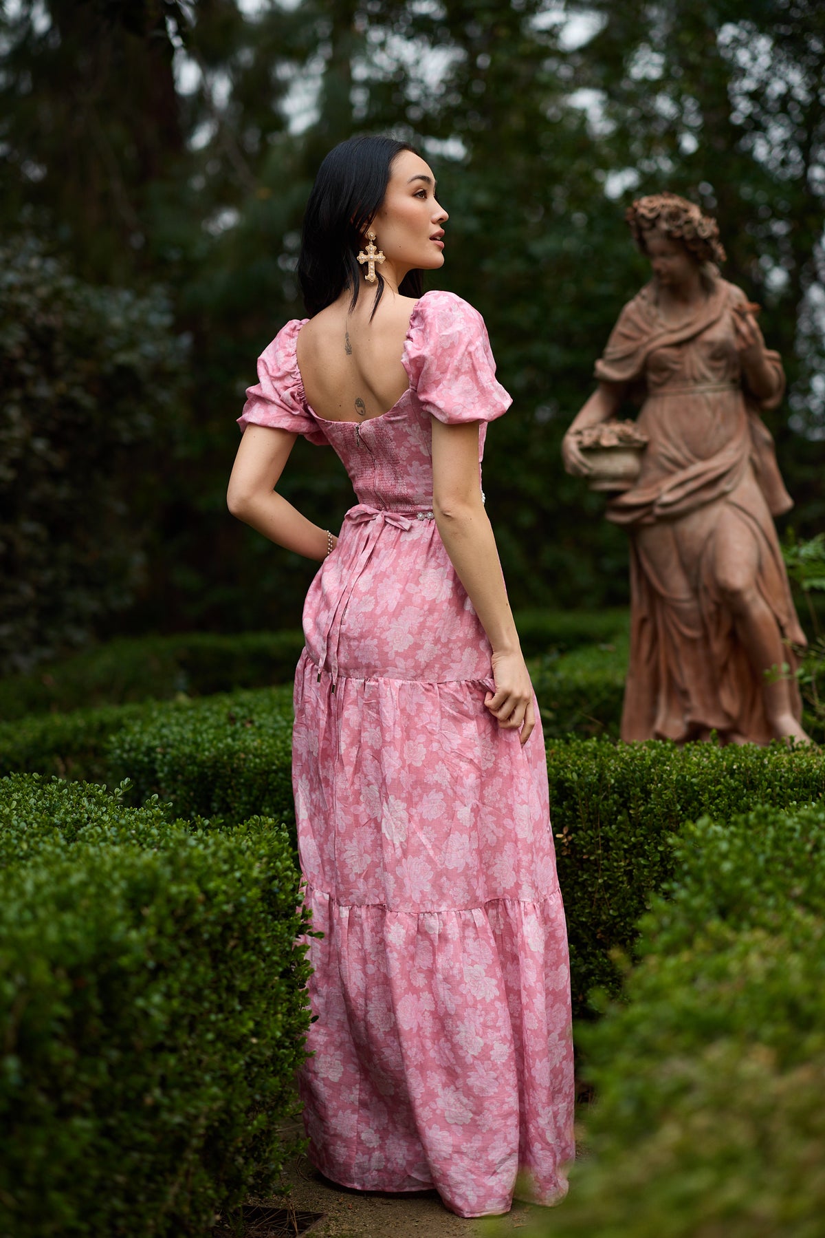 Back view of The Emma Dress in Pink Peony Print showcasing puff sleeves and ruched back panel in a garden