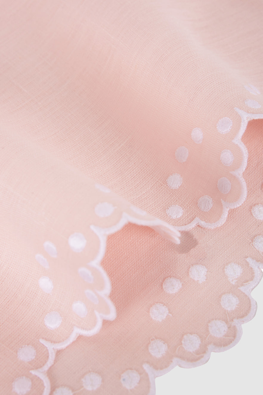 Close-up of Bodoques linen napkin showcasing scalloped embroidered edge and white dotted embroidery on pale pink linen