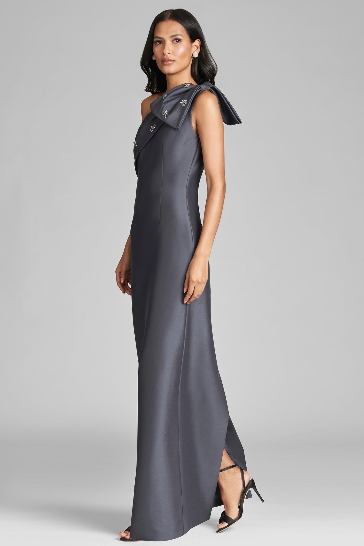 Front view of Olivia Gown in Charcoal showcasing one shoulder, half bow, and embellished neckline with gray background