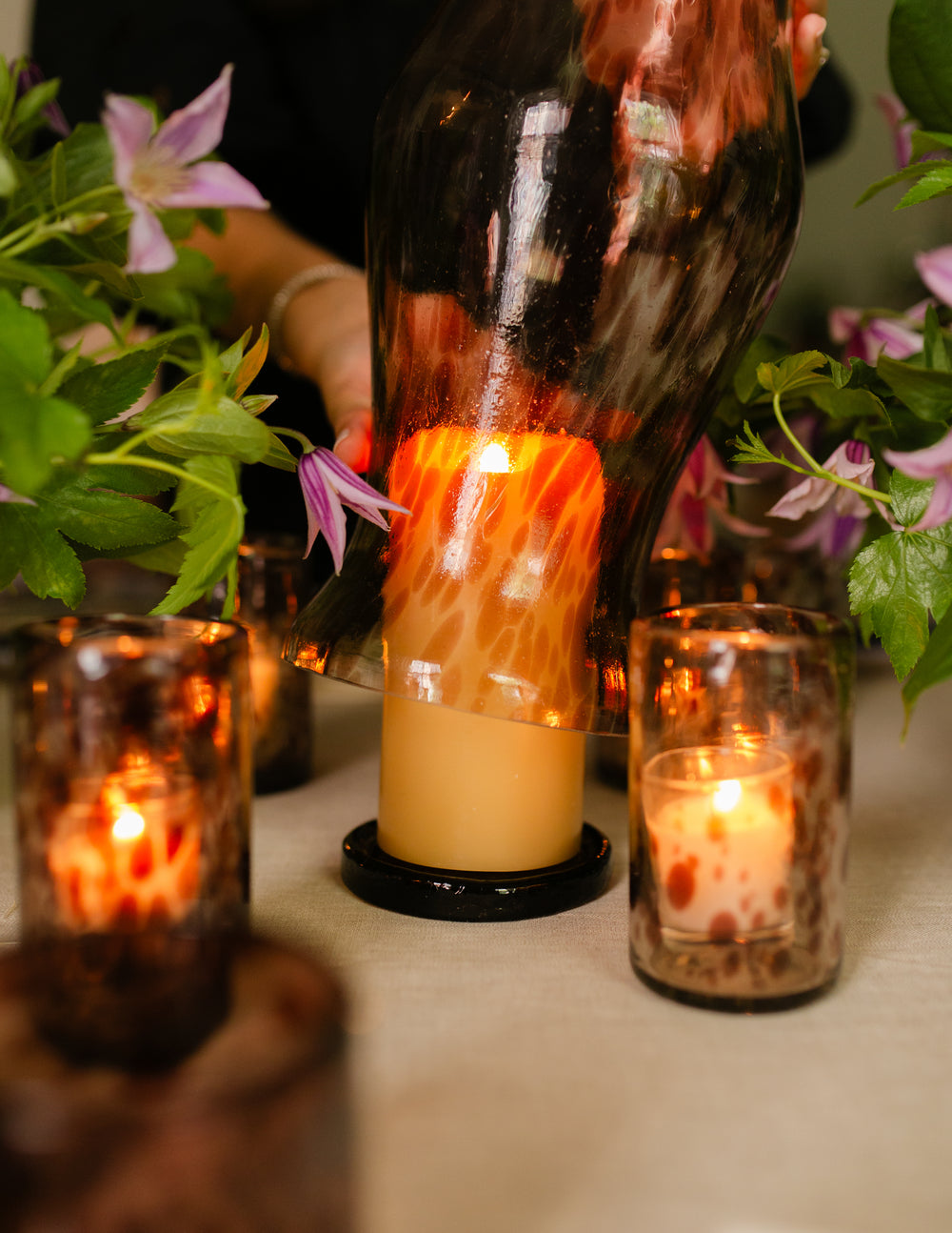 Close-up of olive glass trivet showing marbled recycled-glass finish under a lit pillar candle in a hurricane