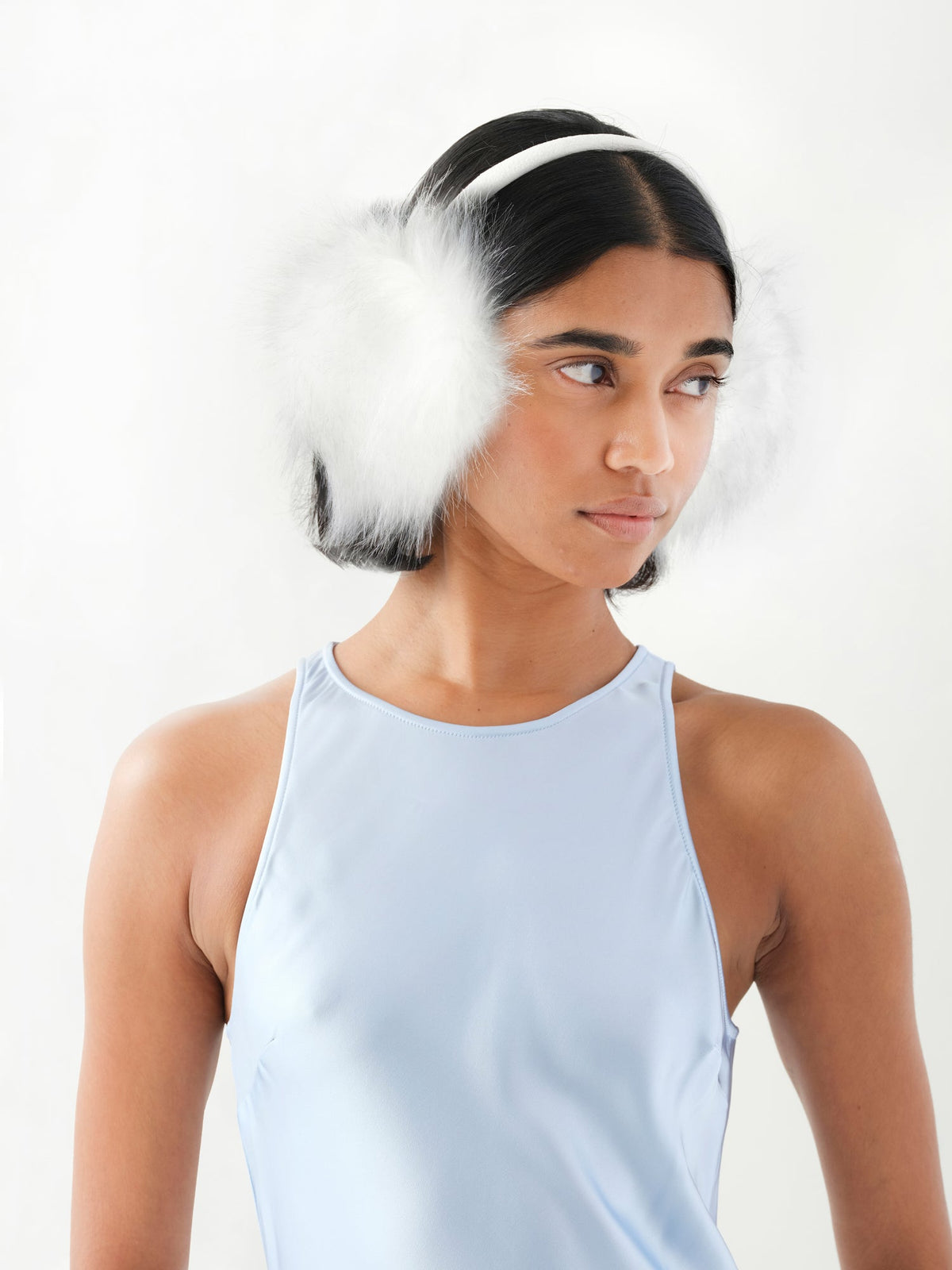 A model in three-quarter view wearing white faux fur earmuffs.