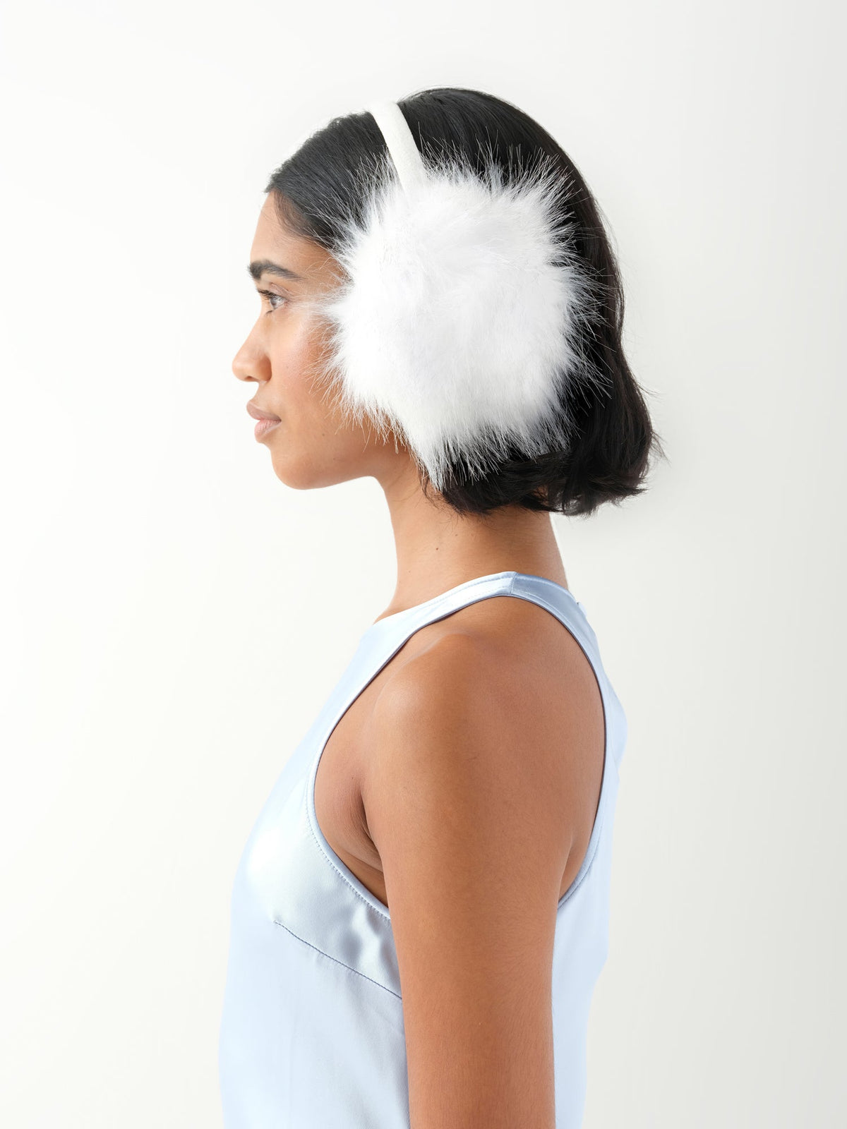 A model in side profile wearing white faux fur earmuffs.