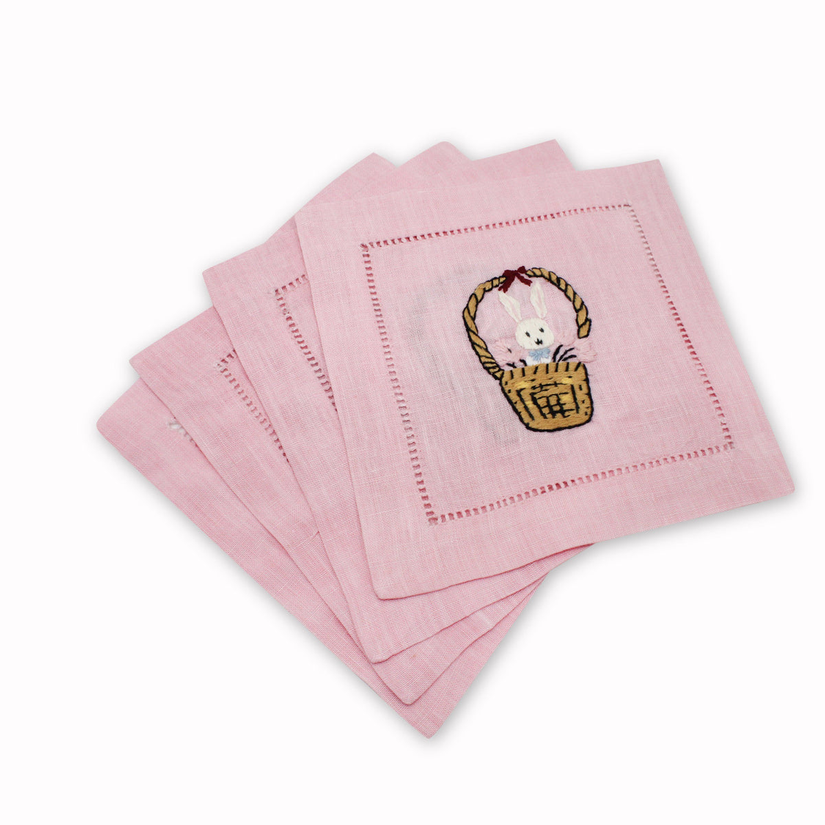 Angled view of Bunny Basket Cocktail Napkins, Set of 4 showcasing embroidered bunny in a basket on pink linen with white background
